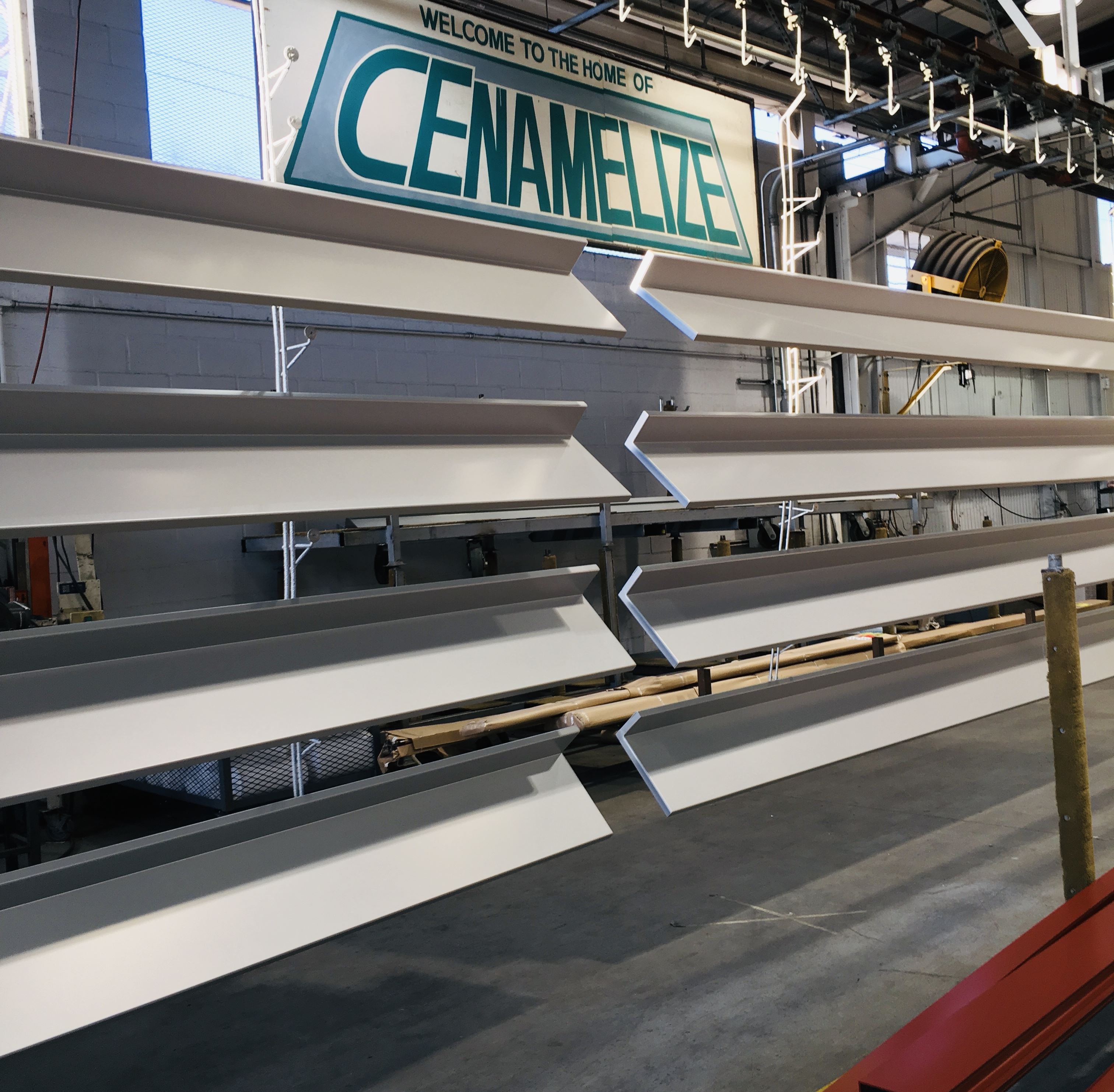 Metal beams in racks under a sign that says, "Welcome to the home of Cenamelize"